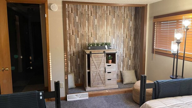 Ein Hotelzimmer mit einer Holzvertäfelung, einem kleinen Schrank mit Pflanzen, einem Fenster mit Jalousien und einem Bett mit gestreifter Bettdecke.