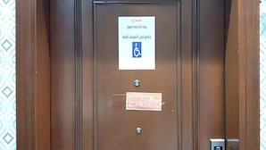 Una puerta marrón con el distintivo de accesibilidad para personas con discapacidad, un cerrojo de seguridad y una cerradura.