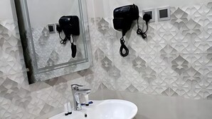 Un baño con un lavabo blanco, un espejo y dos secadores de pelo fijados en la pared.