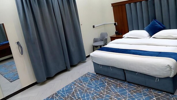 Una habitación de hotel con una cama, una silla, una mesita de noche y una cortina.