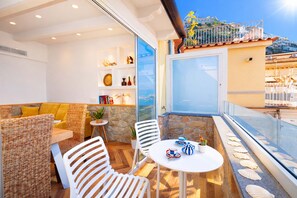 A balcony with wicker furniture, a white table with cups, and a stone wall. - Appartamento Seapearl Sorrento (Sorrento)