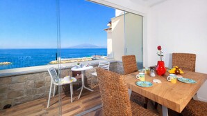 Un'area pranzo con tavolo imbandito per quattro persone, un'ampia finestra vista mare e sedie in vimini.