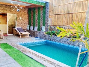 A swimming pool with a stone border, a wooden deck, and a bamboo fence. - Charming House with Private Pool (Bacolod City)