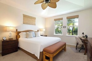 Ein Schlafzimmer mit einem Bett, Nachttischen, einem Schreibtisch, einem Sessel, einem Deckenventilator und Fenstern mit Blick auf Grünflächen.