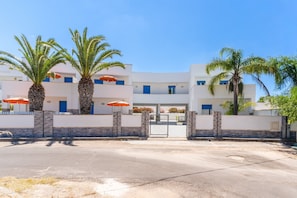 A modern building with a white facade, blue doors, and palm trees. - Apartment 'Residence La Perla - Rubino' with Balcony and Air Conditioning (Marina di Mancaversa)