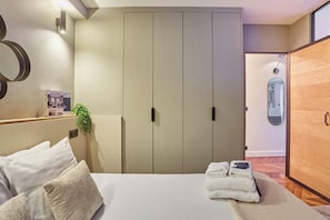 Une chambre à coucher avec un lit, des oreillers, une table de chevet, un miroir, une armoire et une petite plante.