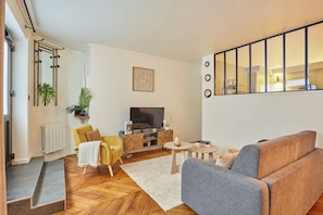 Un salon moderne avec un canapé, un fauteuil, une télévision et une grande fenêtre.