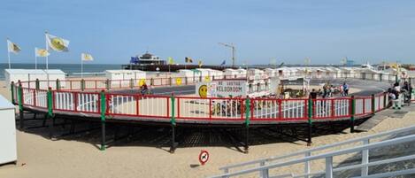 A beachside pier with a red and white railing, a sign reading "BE LOSTIC VELODROOM," and a boat docked in the background.