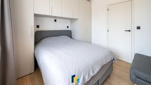 Un dormitorio con cama, sofá gris y paredes blancas.