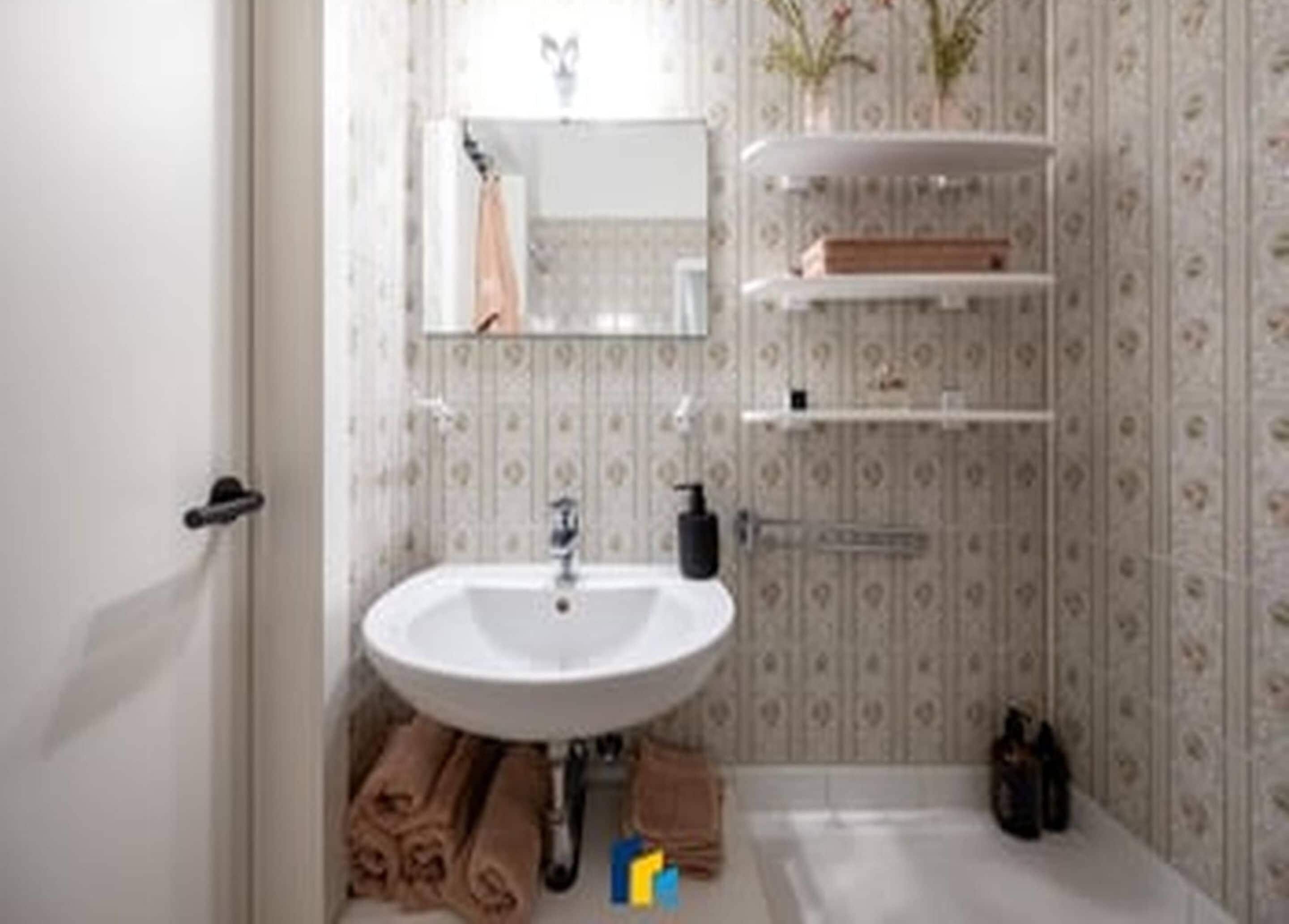 Un bagno con un lavandino bianco, uno specchio e un porta asciugamani.