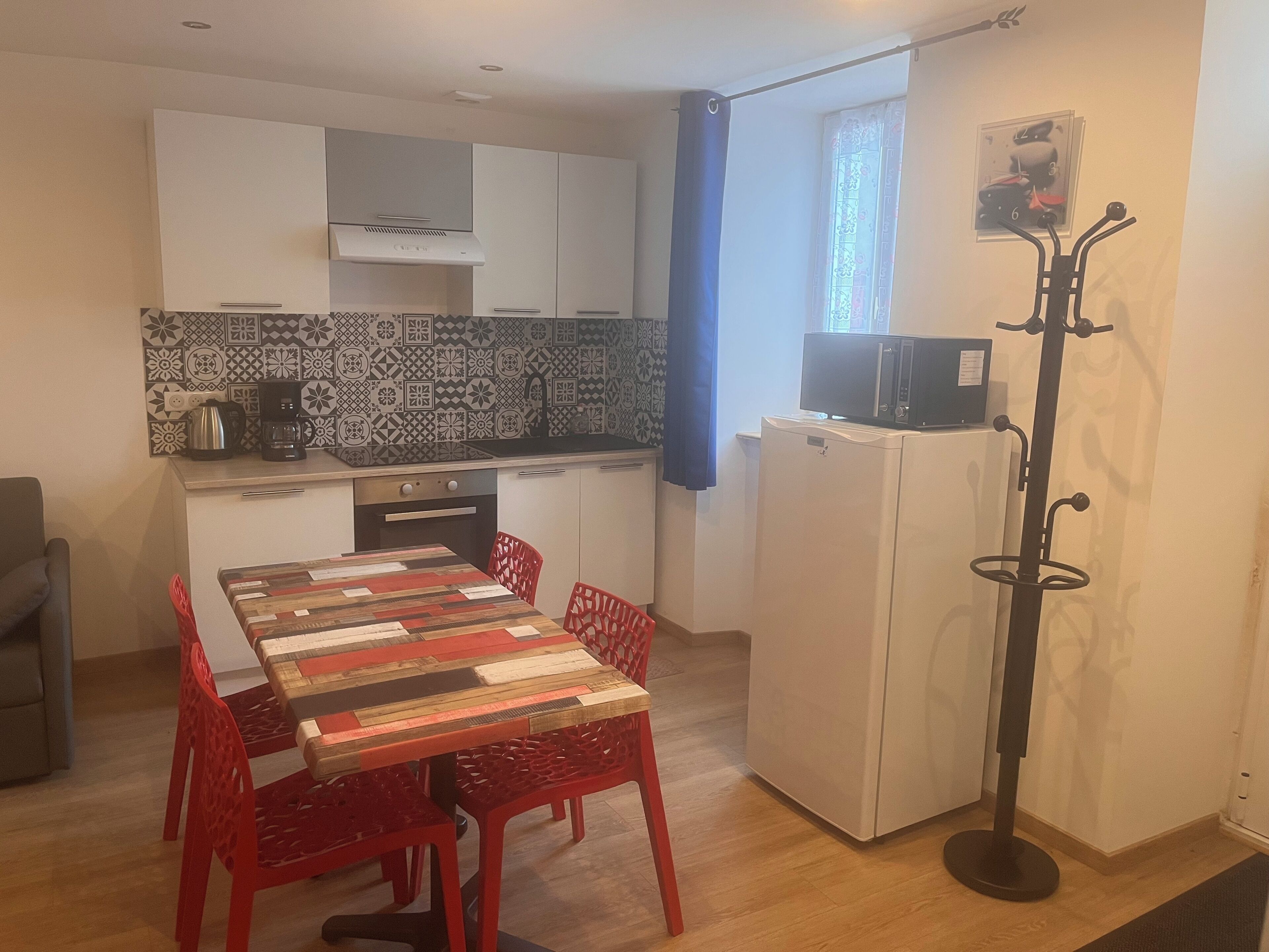 Cozinha compacta com painel decorativo, micro-ondas sobre uma geladeira branca, e mesa de jantar com cadeiras vermelhas.