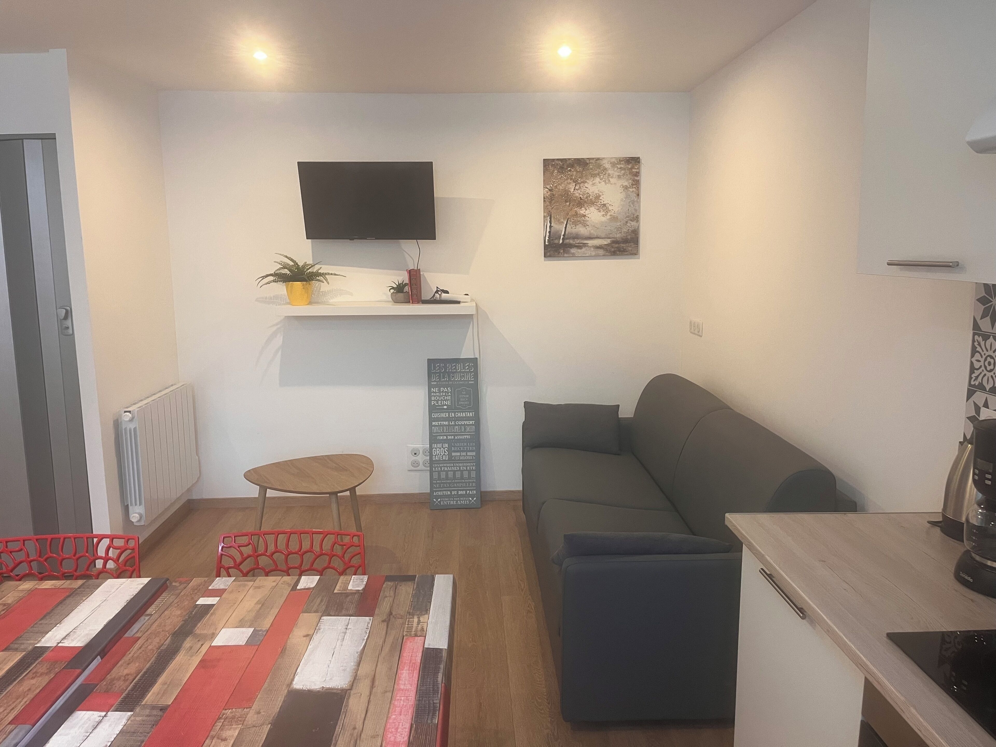 Een moderne woonkamer met een bank, een bijzettafeltje, een flatscreen televisie aan de muur en een decoratief object erboven.