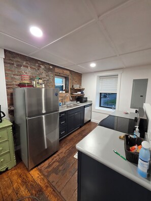 A modern kitchen with a stainless steel refrigerator, wooden flooring, and a brick accent wall.