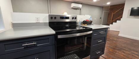 A kitchen with a built-in oven, a microwave, and a range hood. There is a wooden floor and a white countertop.