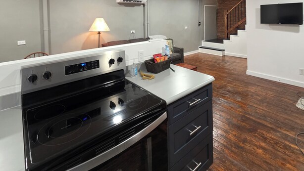 A modern kitchen with a built-in oven, a stove, and a microwave. There is a wooden floor, a staircase leading to another level, and a flat-screen TV mounted on the wall. - 2nd story fully furnished apartment-walk everywhere & one block from river/park (Vevay)