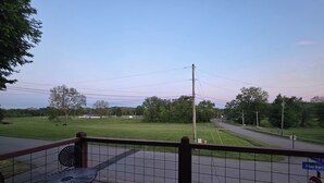 A wooden deck with a metal table and chairs, a stop sign, and a view of a road and green fields. - 2nd story fully furnished apartment-walk everywhere & one block from river/park (Vevay)
