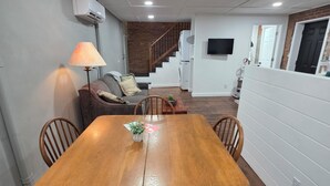 A dining area with a wooden table and chairs, a lamp, a sofa, and a staircase leading to another level. - 2nd story fully furnished apartment-walk everywhere & one block from river/park (Vevay)