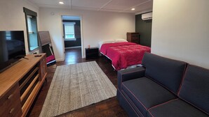 A room with a bed, a TV, a wooden dresser, a red bedspread, and a black couch. - 2nd story fully furnished apartment-walk everywhere & one block from river/park (Vevay)