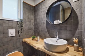 Ein modernes Badezimmer mit rundem Spiegel, Holztischplatte und weißem Waschbecken.