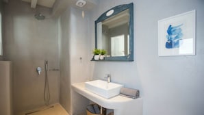 Un baño con ducha, lavamanos, espejo y un cuadro en la pared.