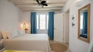 Un dormitorio con cama, ventilador de techo, lámpara de noche, ventana con cortinas y puerta.