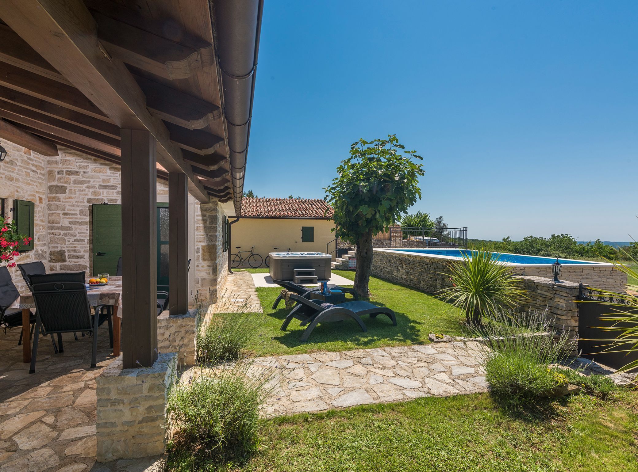 A stone building with a patio, outdoor seating, a hot tub, and a swimming pool.