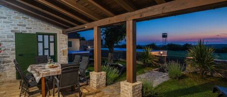 A stone patio with outdoor seating, a hot tub, and a view of the landscape at dusk.