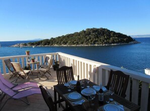 Une terrasse avec une table dressée pour le dîner, offrant une vue sur une étendue d’eau et une petite île.