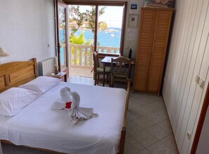 A hotel room with a bed, a wooden headboard, a wooden wardrobe, a dining table with chairs, and a view of the sea through an open door. - Apartments Villa Maria (Lastovo)