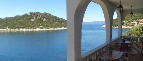 A balcony with a view of a calm sea and a hilly landscape.