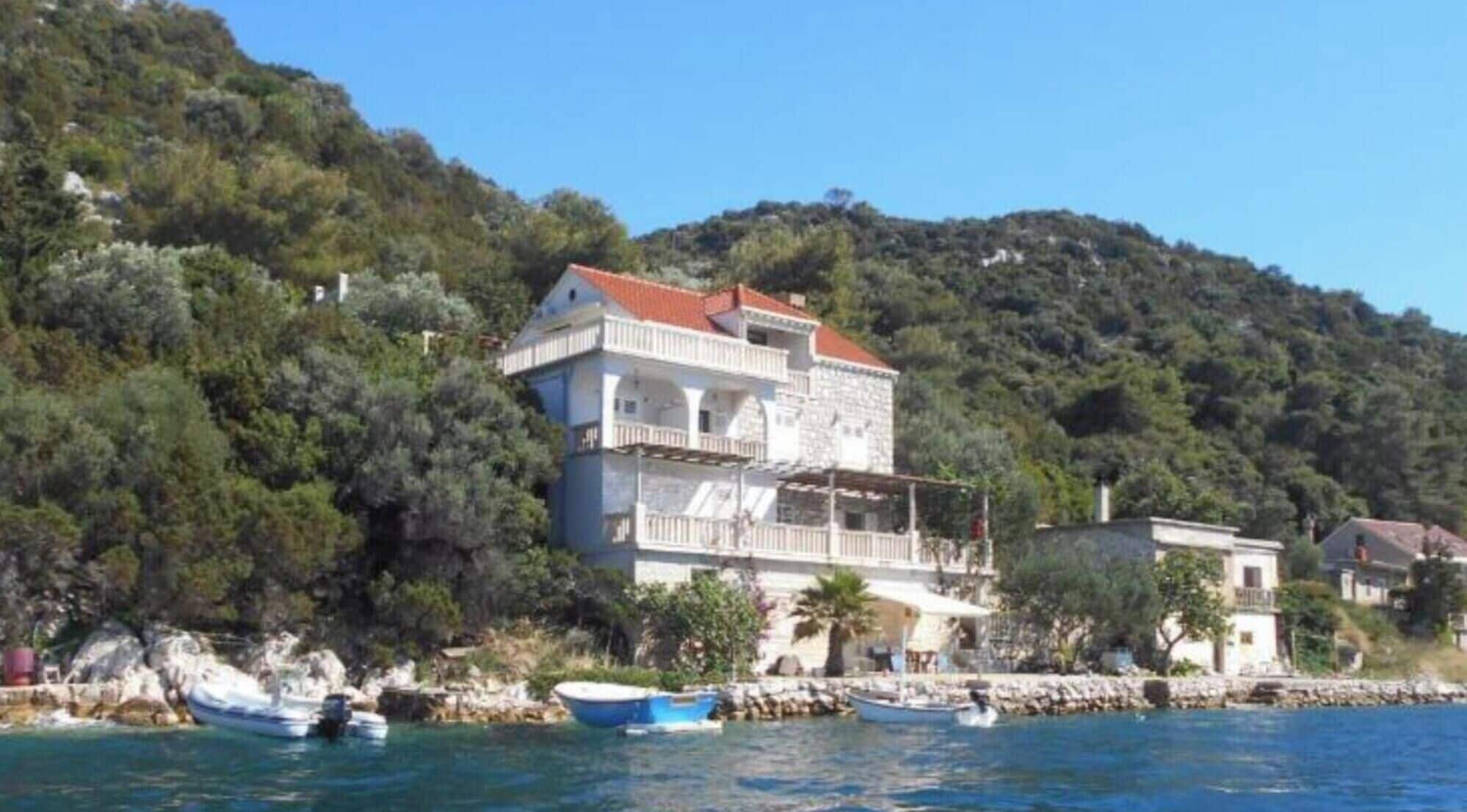 A coastal building with a red roof, white walls, and balconies.