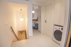 Ein Flur mit einer Waschmaschine, einem Bett und einer Tür zu einem weiteren Zimmer.