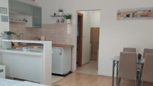 A modern kitchen with white cabinets, a refrigerator, and a dining area with a table and chairs. - Boutique Studio Pula (Pula)