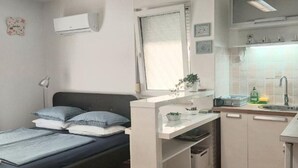 A compact room with a bed, a small kitchenette, a window with curtains, and a wall-mounted air conditioner. - Boutique Studio Pula (Pula)