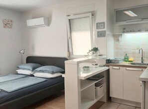 A compact room with a bed, a small kitchenette, a window with curtains, and a wall-mounted air conditioner. - Boutique Studio Pula (Pula)
