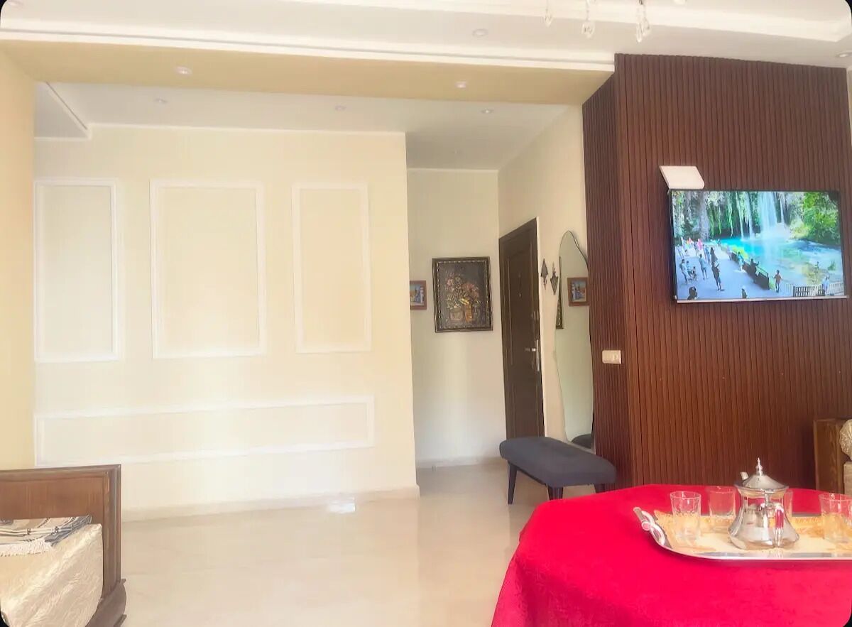 Une chambre d’hôtel avec une télévision, une table à manger recouverte d’une nappe rouge et un banc.