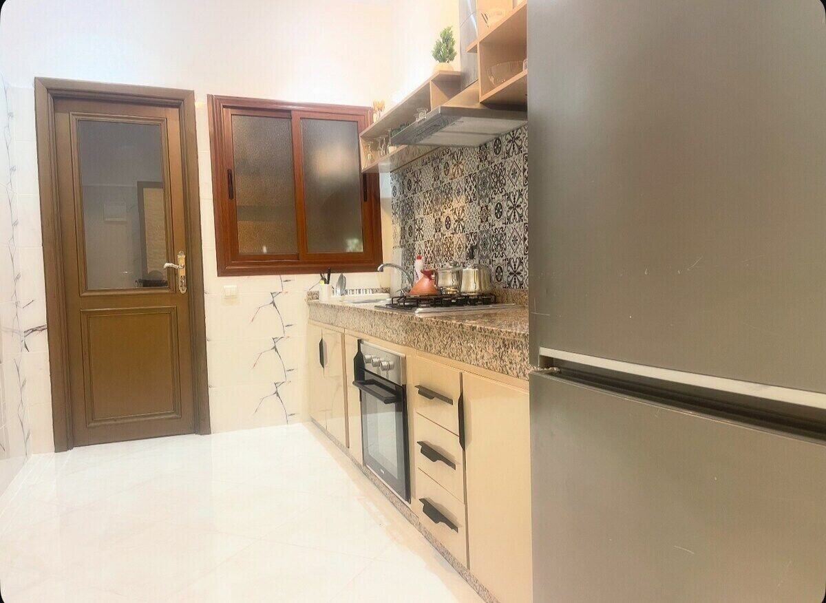 A kitchen with a stainless steel refrigerator, a stove, and a microwave. There are wooden cabinets and a tiled backsplash.