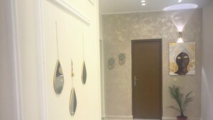 A hallway with a door, a wall-mounted light fixture, and a potted plant. - Modern Wi-Fi, Agadir, 10 min Beach, Netflix, IPTV, First floor. 93m2. Balcony. (Agadir)