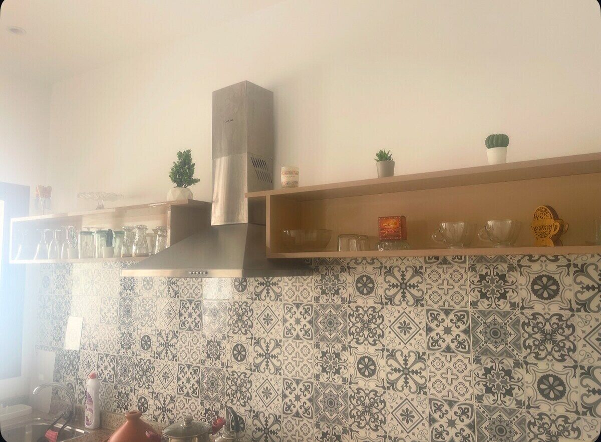 Keittiössä on kuvioituja laattoja, ruostumattomasta teräksestä valmistettu liesituuletin sekä hyllyjä, joilla on esillä lasiesineitä ja koriste-esineitä.