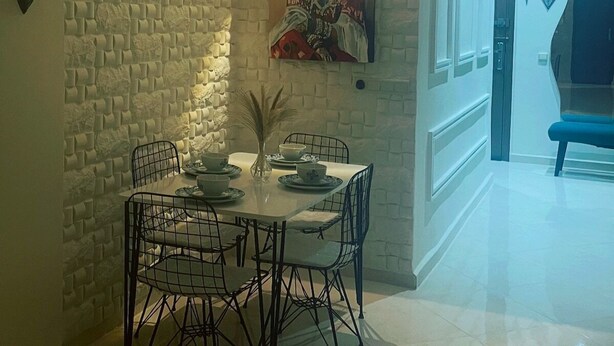 A dining area with a stone wall, a painting, and a table set for four. - Modern Wi-Fi, Agadir, 10 min Beach, Netflix, IPTV, First floor. 93m2. Balcony. (Agadir)