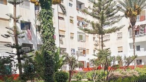 A residential building with balconies, surrounded by a garden with various plants and a metal fence. - Modern Wi-Fi, Agadir, 10 min Beach, Netflix, IPTV, First floor. 93m2. Balcony. (Agadir)