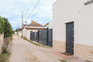 A narrow street with a gravel path, a black metal fence, and a building with a white facade and a black door. - Spacious Studio 2P - Benerville (Benerville-sur-Mer)