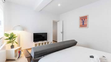 A hotel room with a bed, a TV, a lamp, a plant, and a poster on the wall.