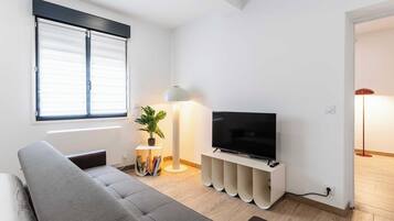 A modern living room with a sofa, a flat-screen TV, a lamp, and a bookshelf.