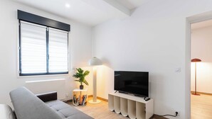A modern living room with a sofa, a flat-screen TV, a lamp, and a bookshelf. - Spacious Studio 2P - Benerville (Benerville-sur-Mer)