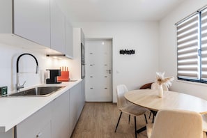 A modern kitchen with a sink, stove, and dining area with chairs and a table. - Spacious Studio 2P - Benerville (Benerville-sur-Mer)
