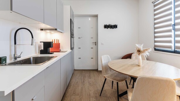 A modern kitchen with a sink, stove, and dining area with chairs and a table. - Spacious Studio 2P - Benerville (Benerville-sur-Mer)