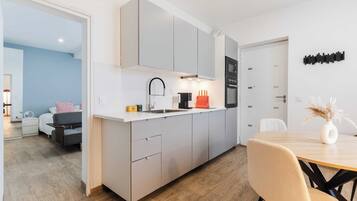 A modern kitchen with grey cabinets, a white countertop, and a dining area with a table and chairs.