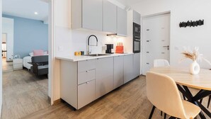 A modern kitchen with grey cabinets, a white countertop, and a dining area with a wooden table and chairs. - Spacious Studio 2P - Benerville (Benerville-sur-Mer)