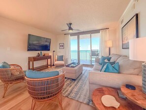 A living room with a sofa, two wicker chairs, a television, a table, and a balcony with a view. - Stunning 3BR/3BA Brighton Tower | Fully Renovated (Myrtle Beach)